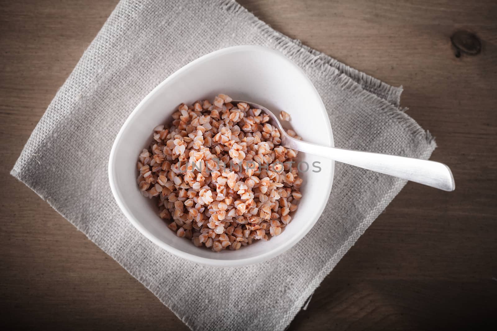 Boiled buckwheat with spoon in ceramic bowl.