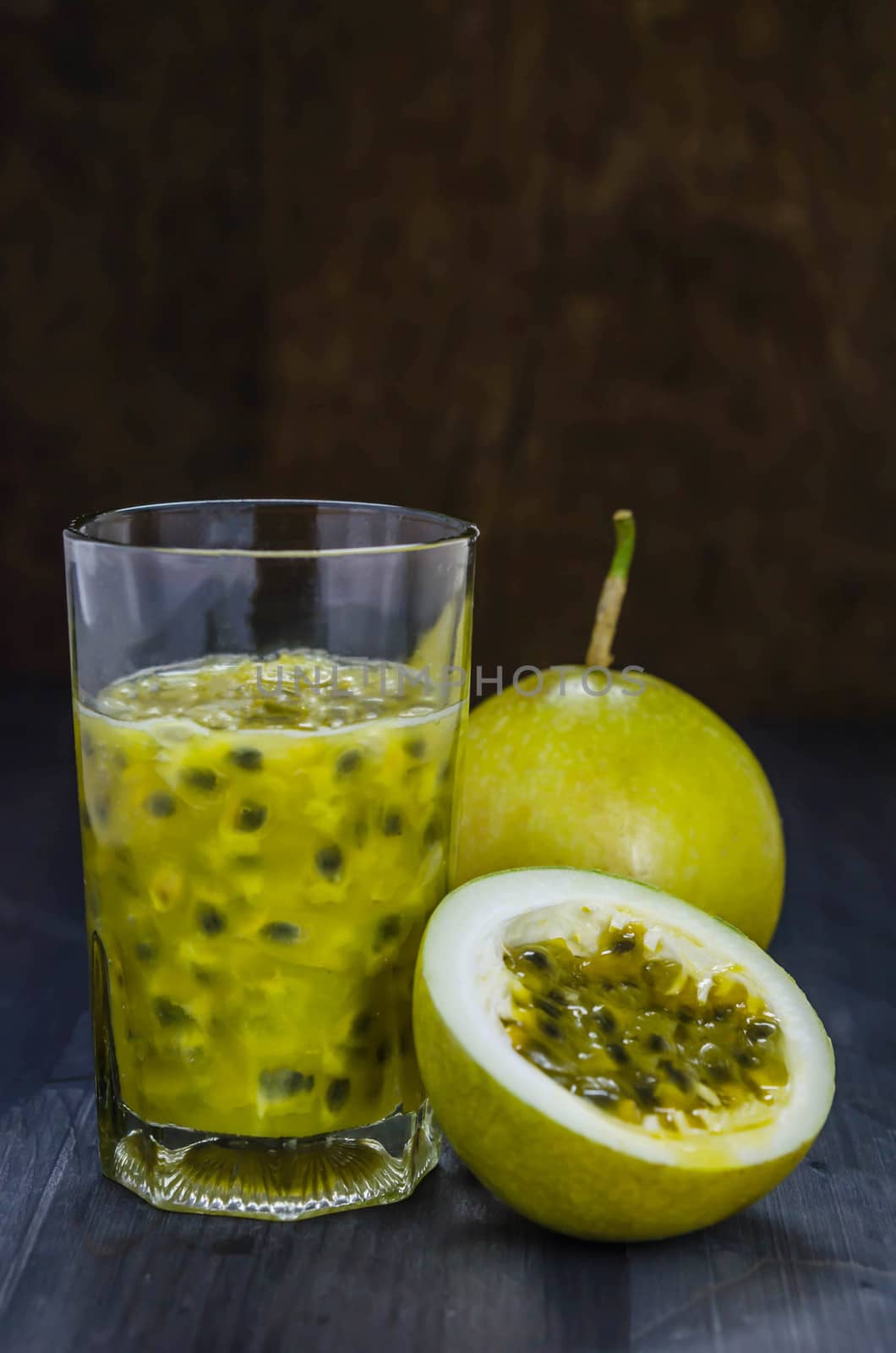 Fresh passion fruit juice in glass with passion fruits over wooden background , still life