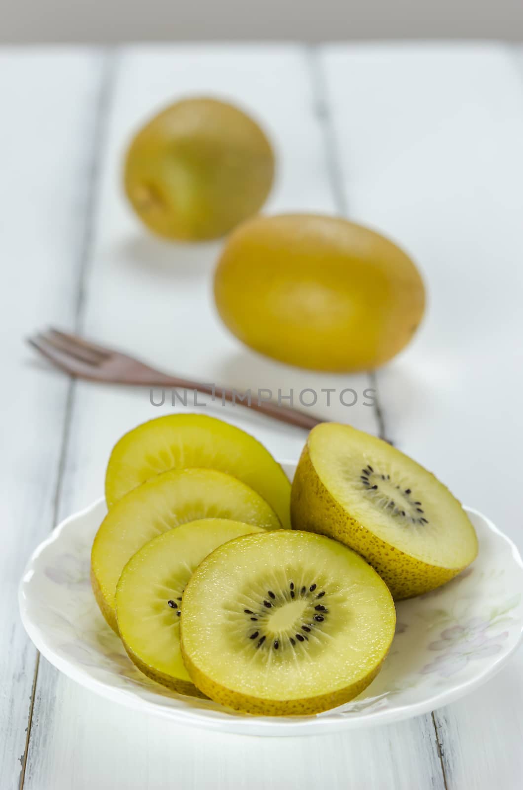 golden kiwi fruit and sliced on dish over white wooden background