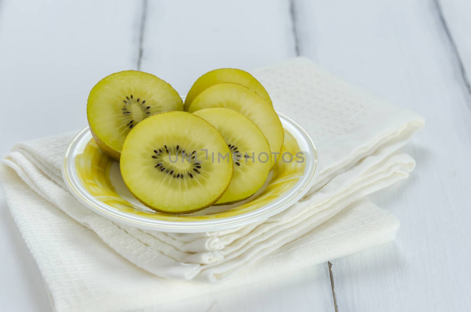 golden kiwi fruit and sliced on dish over white wooden background