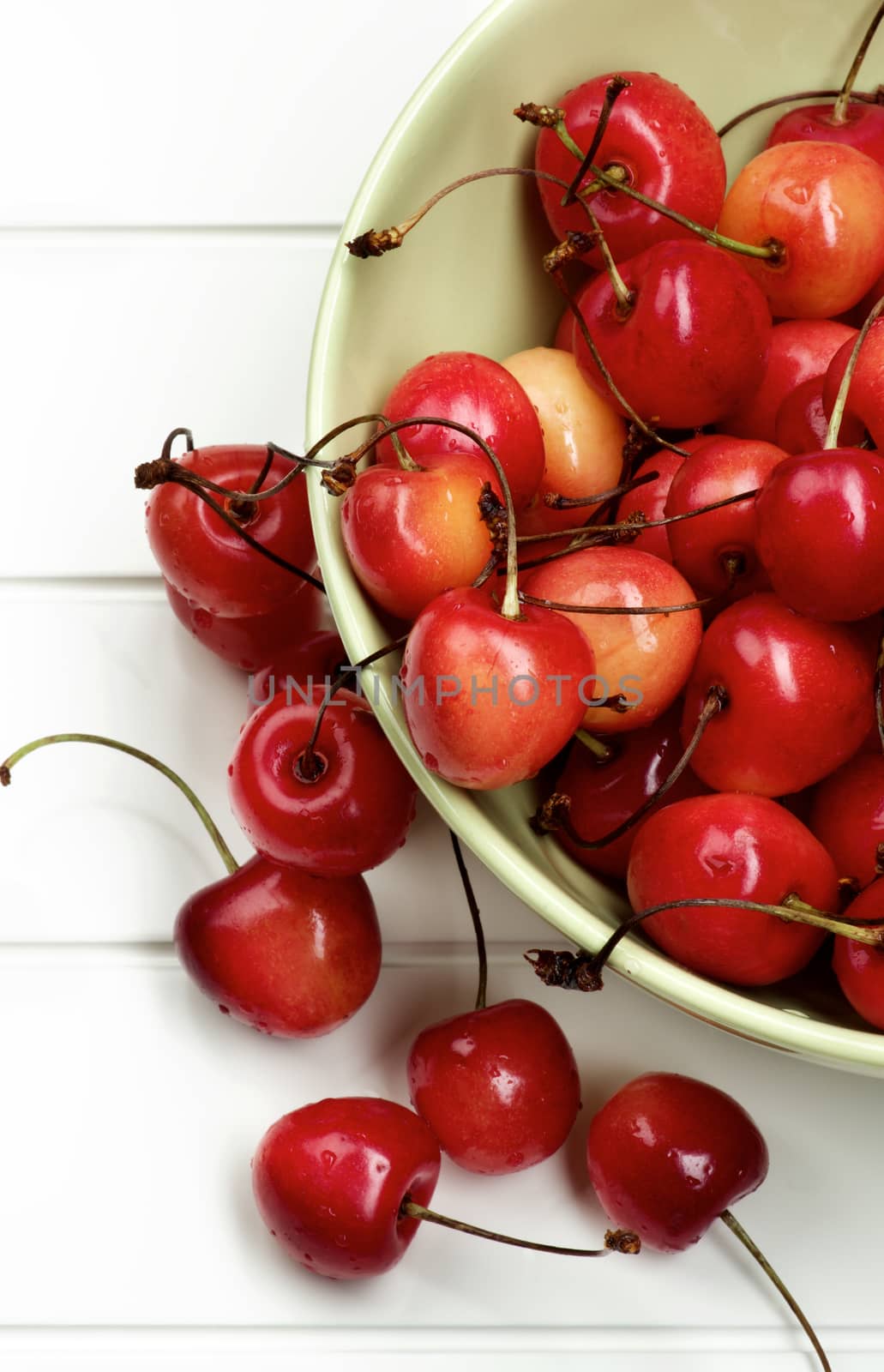 Heap of Fresh Ripe Sweet Maraschino Cherries in Green Bowl Cross Section on Plank White background. Top View