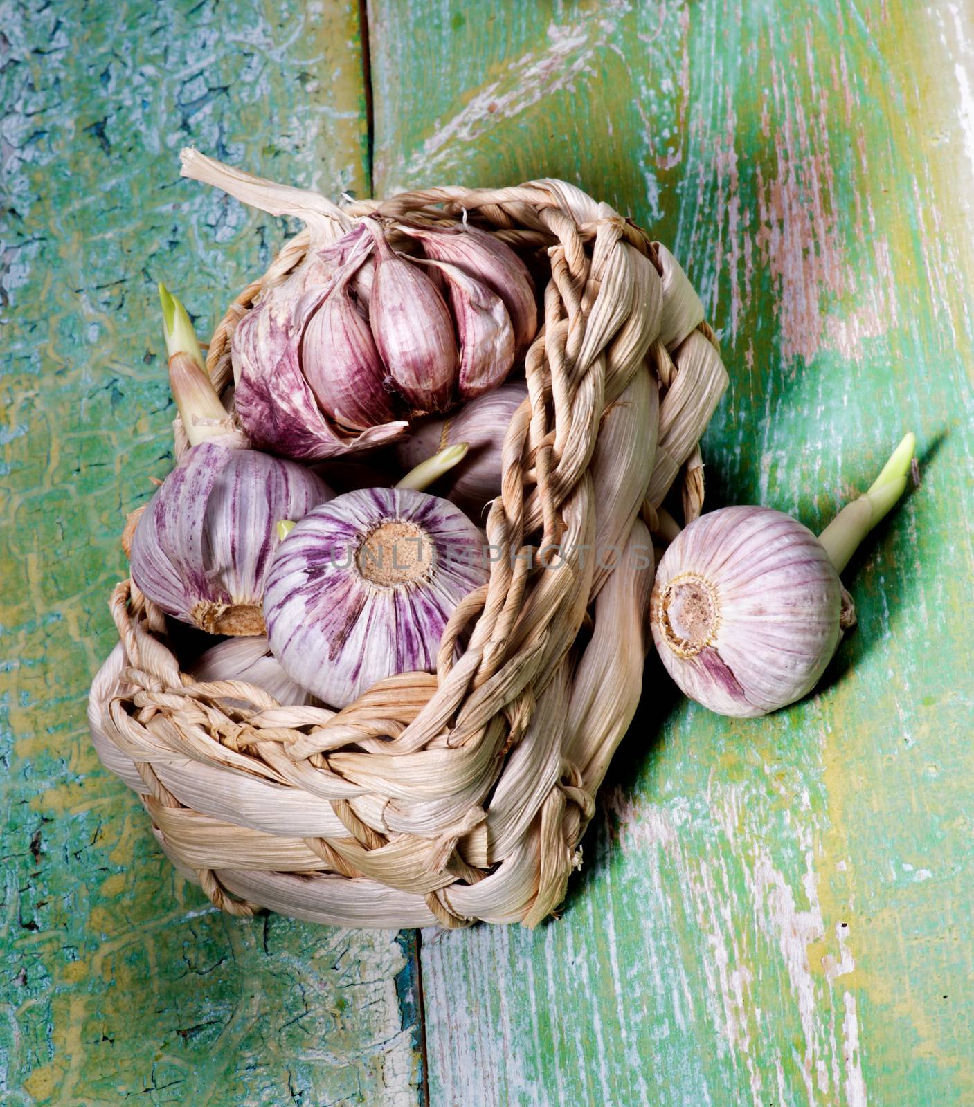 Arrangement of Fresh Pink Garlic with Green Stems in Wicker Basket closeup on Cracked Wooden background