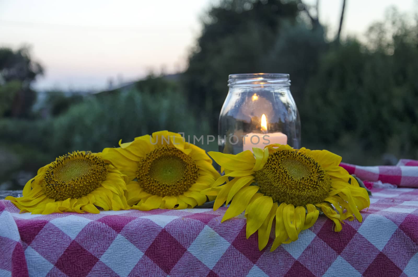 Glass jar with lit candle inside and sunflowers