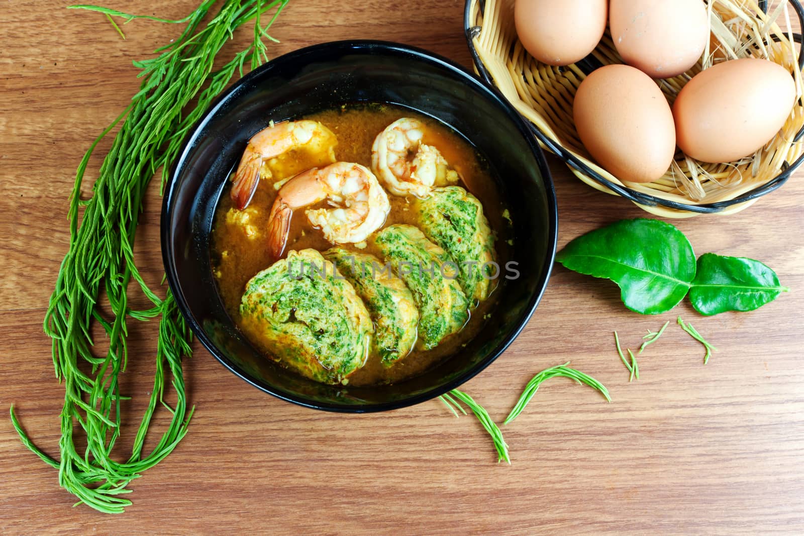 Hot and sour soup curry with shrimps and acacia pennata omelette. In black dish on wood table.