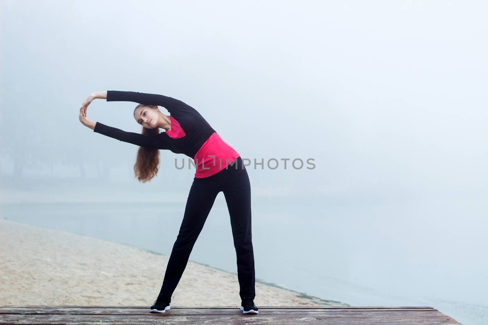 Young pretty slim fitness sporty woman does stretching exercises during training workout outdoor