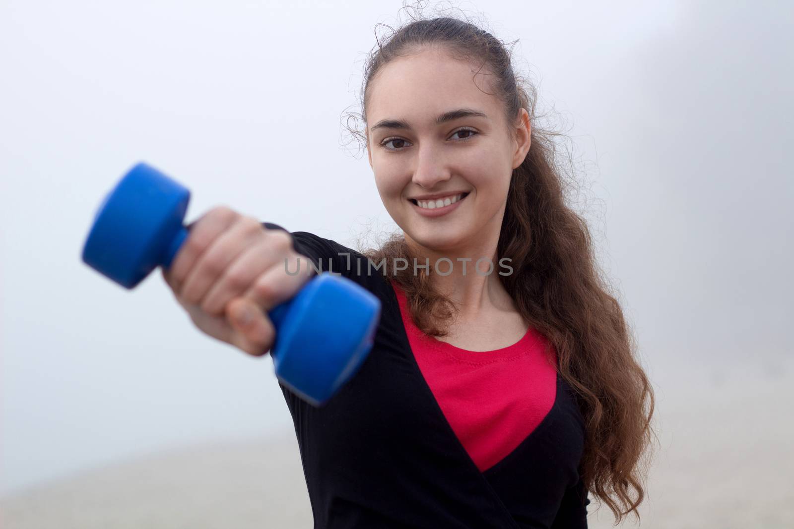 Young pretty slim fitness sporty woman exercises with weights dumbells during training workout outdoor