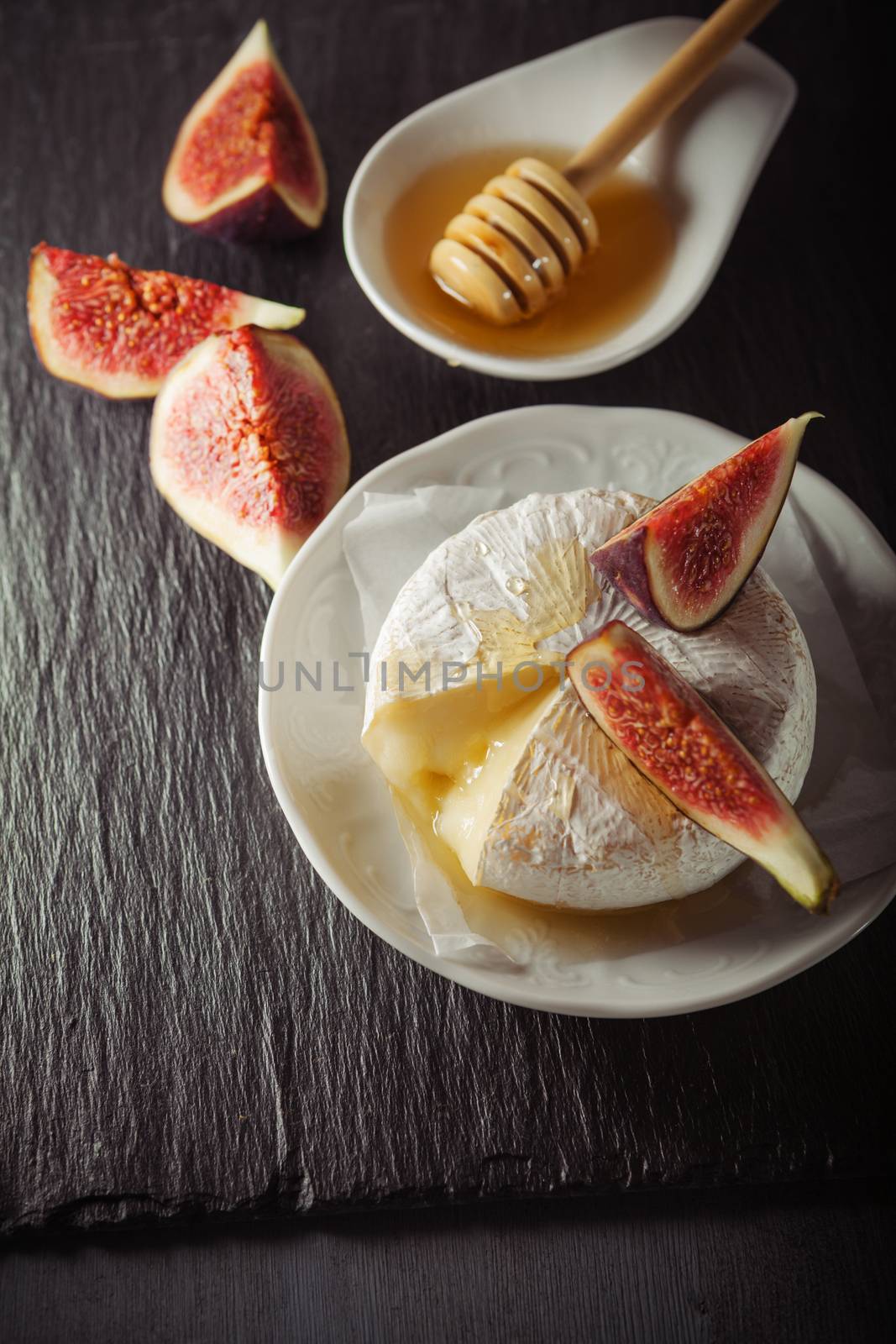 A wheel of melted brie covered in sliced figs and honey  on a stone plate.