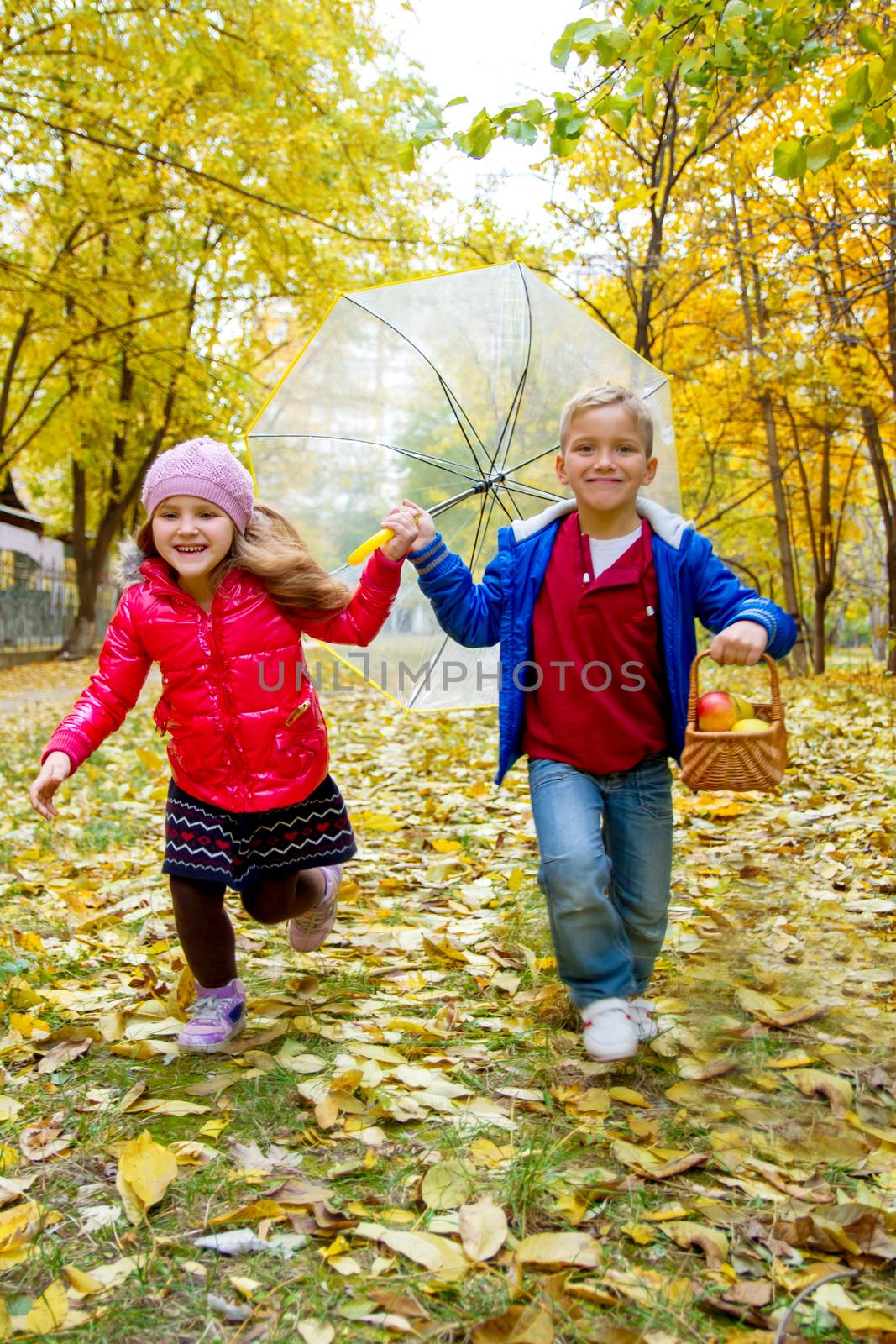 Two children running with umbrella in autumn park