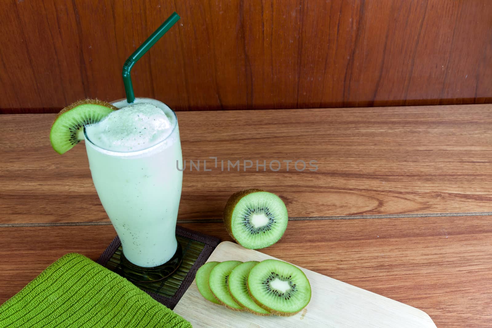 Healthy green smoothie made from kiwi with green straws on a wooden table.