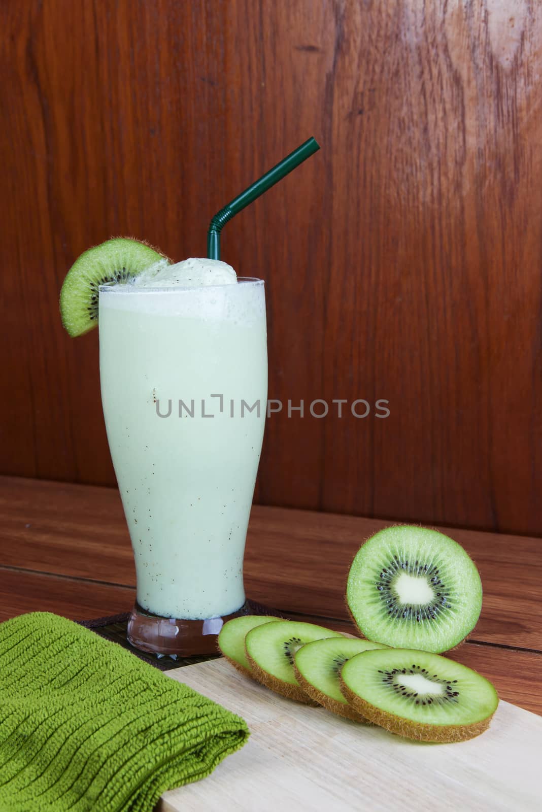 Healthy green smoothie made from kiwi with green straws on a wooden table.