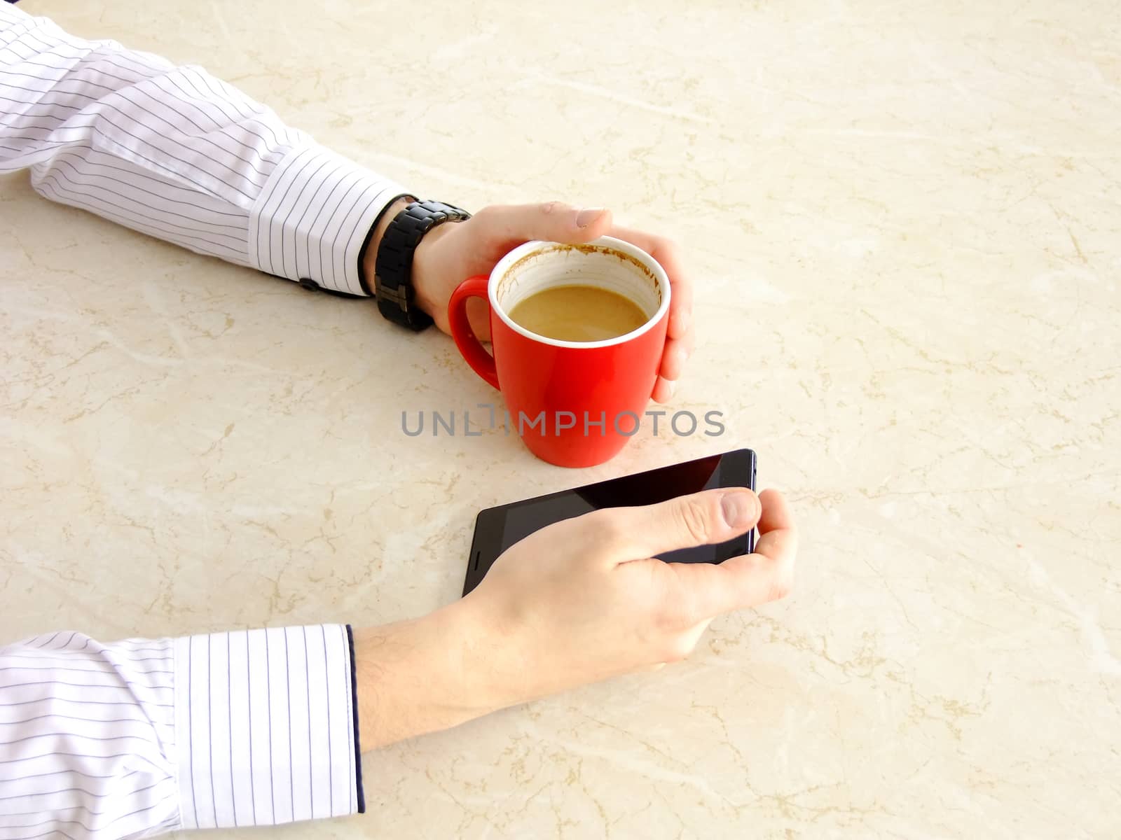 Business man using his Cellphone while holding Coffee in a red Cup