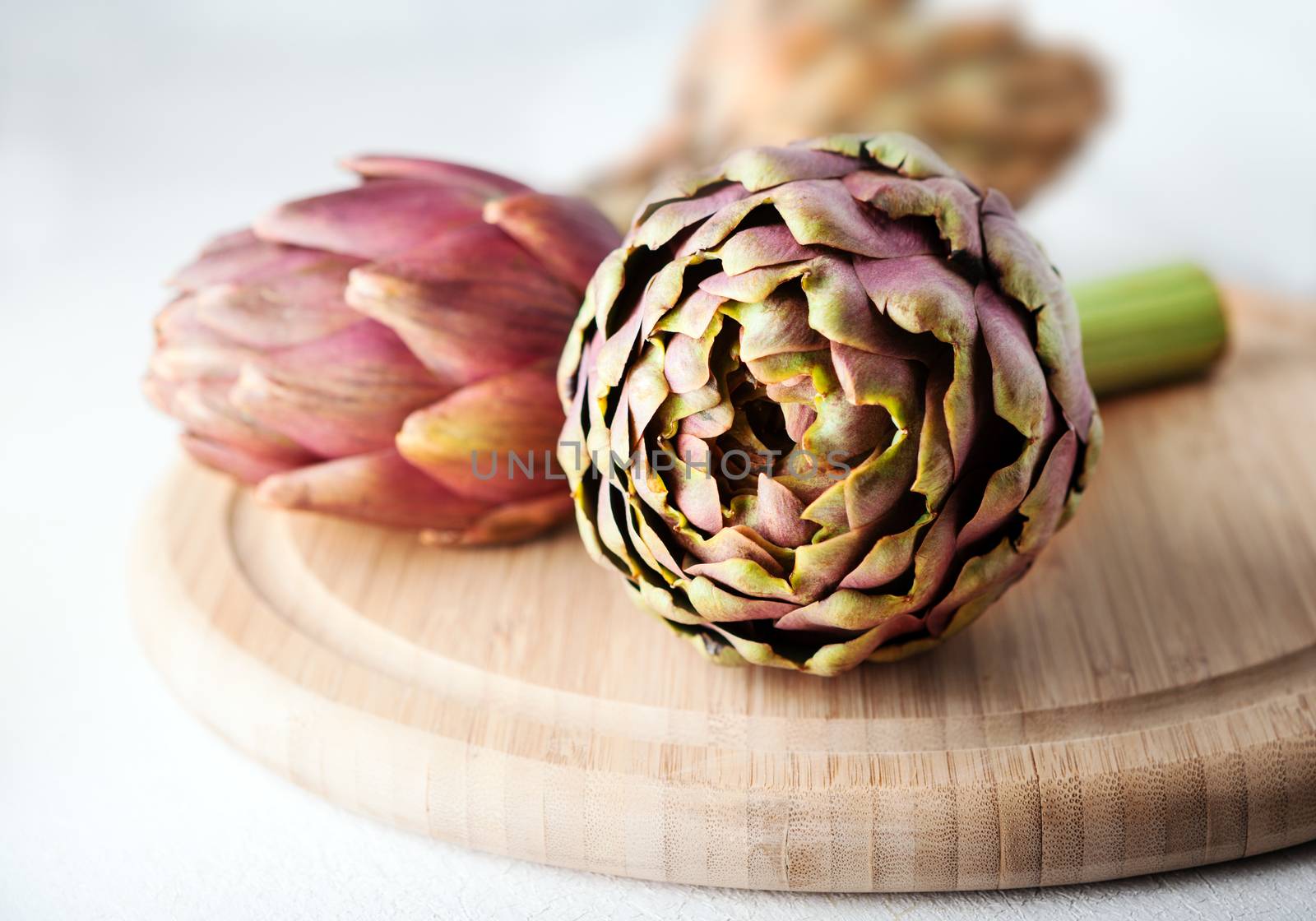 Three artichokes on a wooden cutting board by supercat67