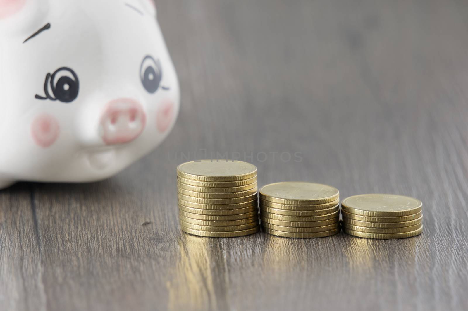 Close up step pile of gold coins have blur piggy bank on wood background.