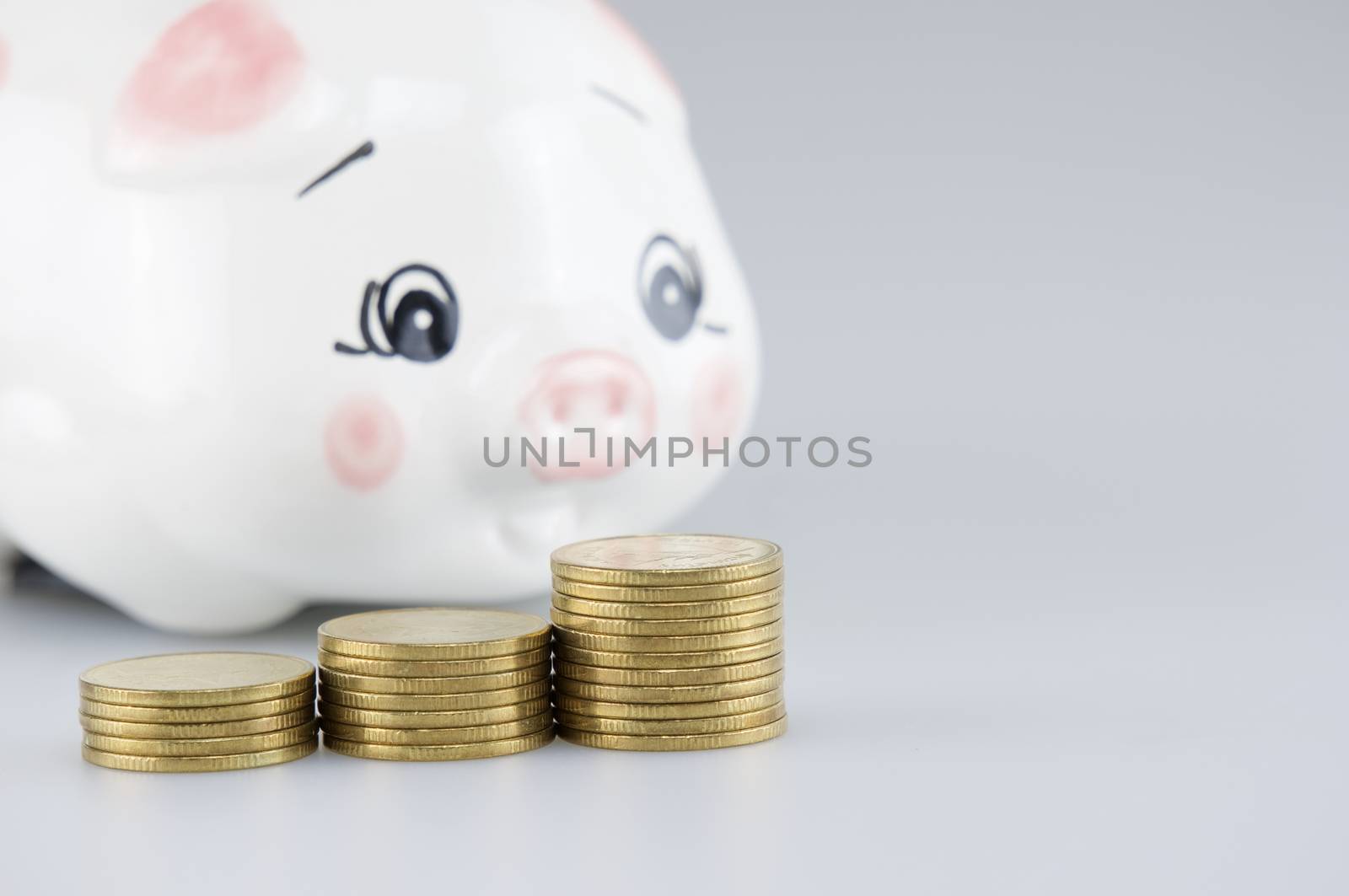 Close up step pile of gold coins have blur piggy bank on white background.