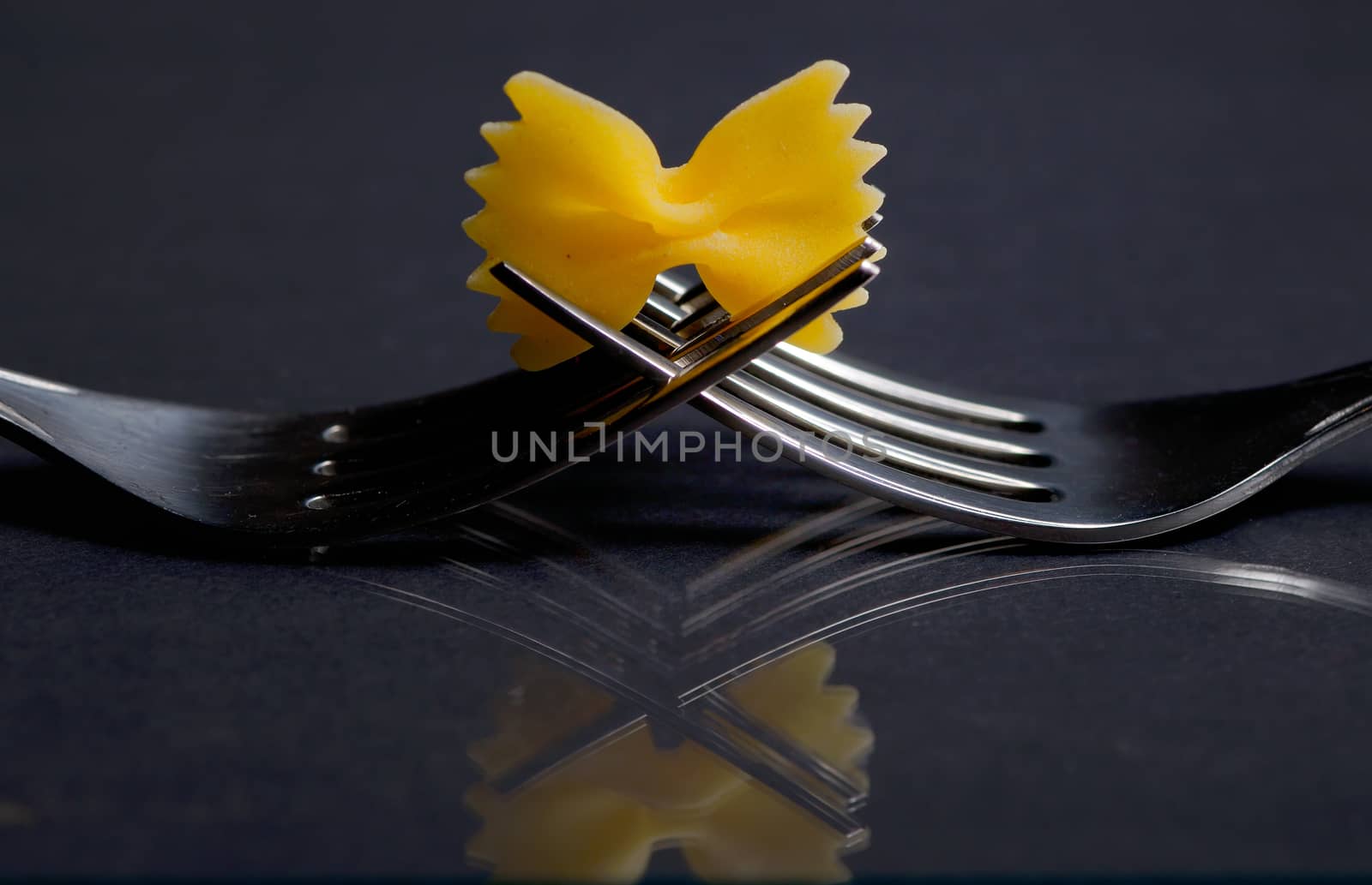 Pasta farfalle on a fork on black background