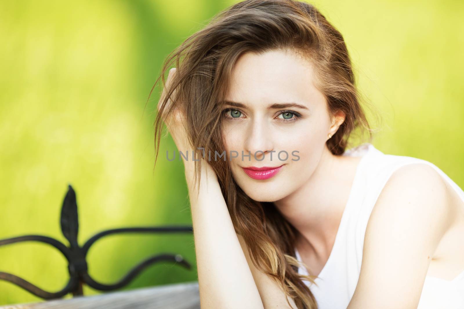 Lovely urban girl sitting on a bench in a city park. Portrait of a happy smiling woman.