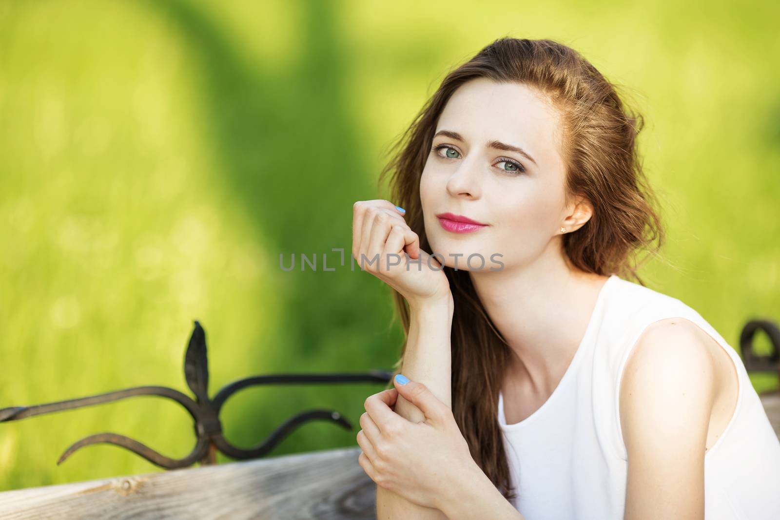 Lovely urban girl sitting on a bench in a city park. Portrait of a happy smiling woman.