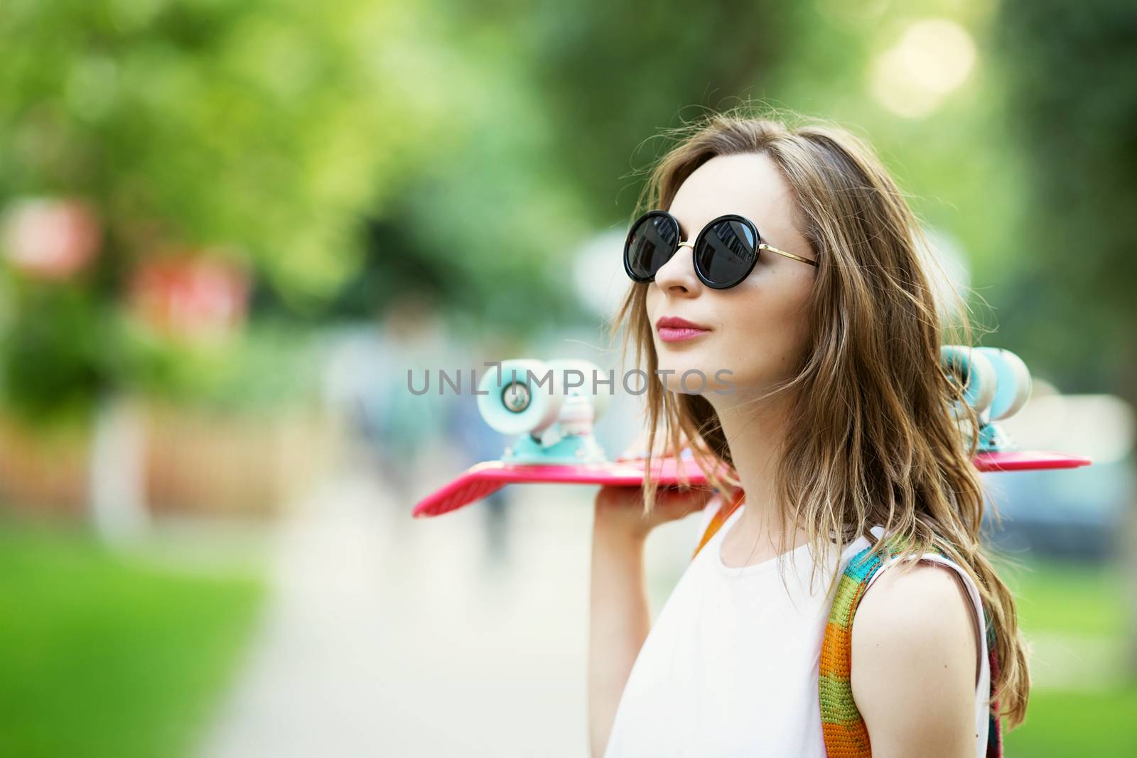 Portrait of lovely urban girl in white dress with a pink skateboard. Happy smiling woman. Girl holding a plastic skate board outdoors. City life.