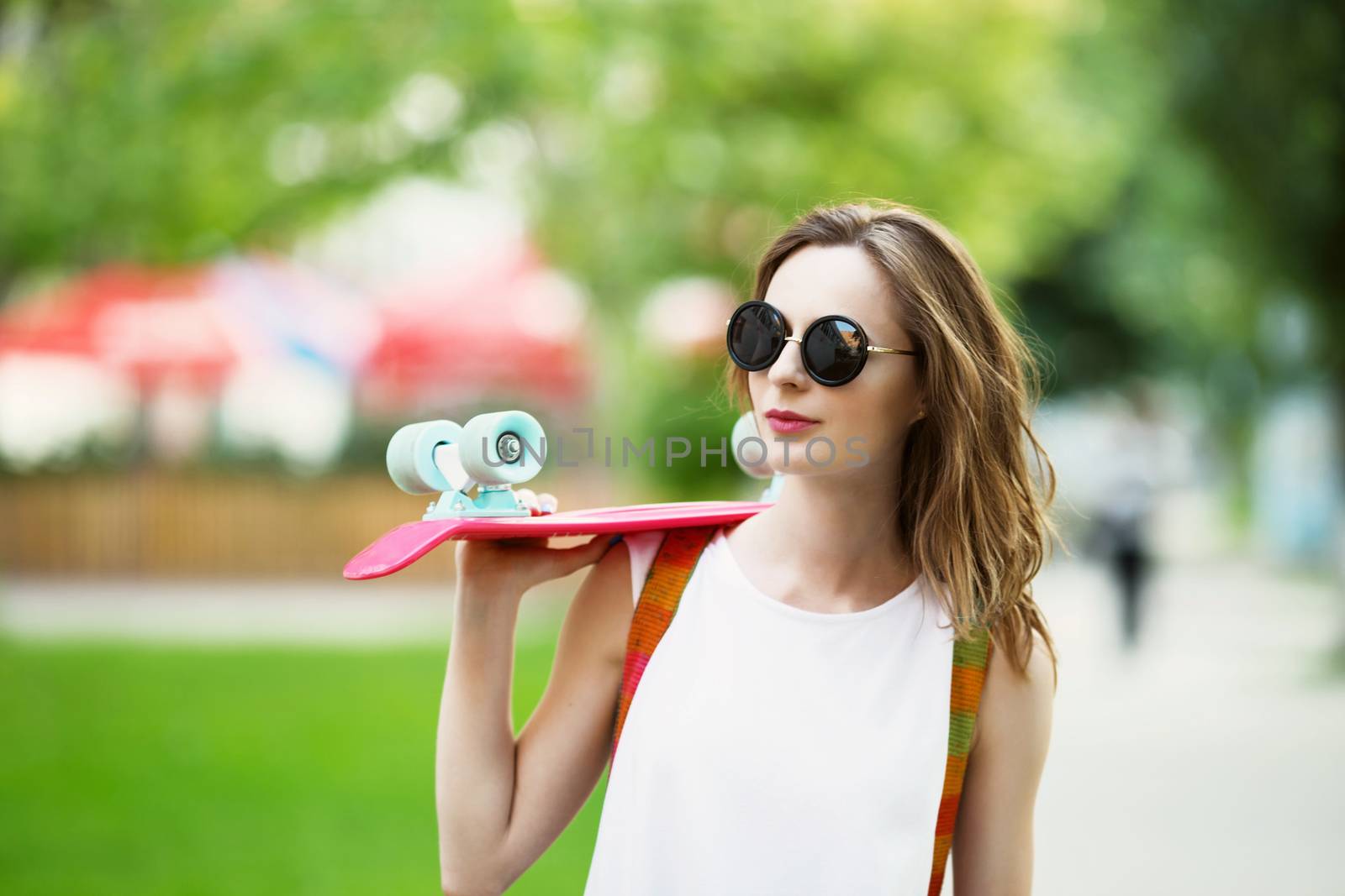 Portrait of lovely urban girl in white dress with a pink skateboard. Happy smiling woman. Girl holding a plastic skate board outdoors. City life.