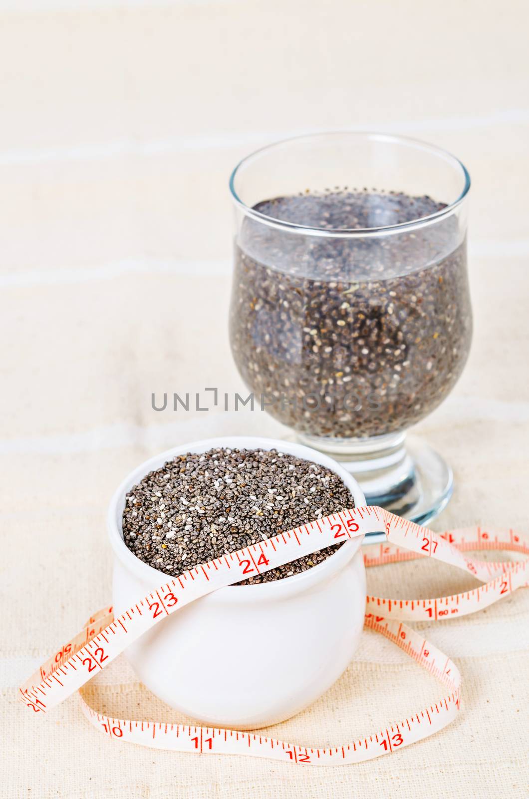 Healthy Chia seeds in white cup and soak in water with measuring tape on tablecloth.