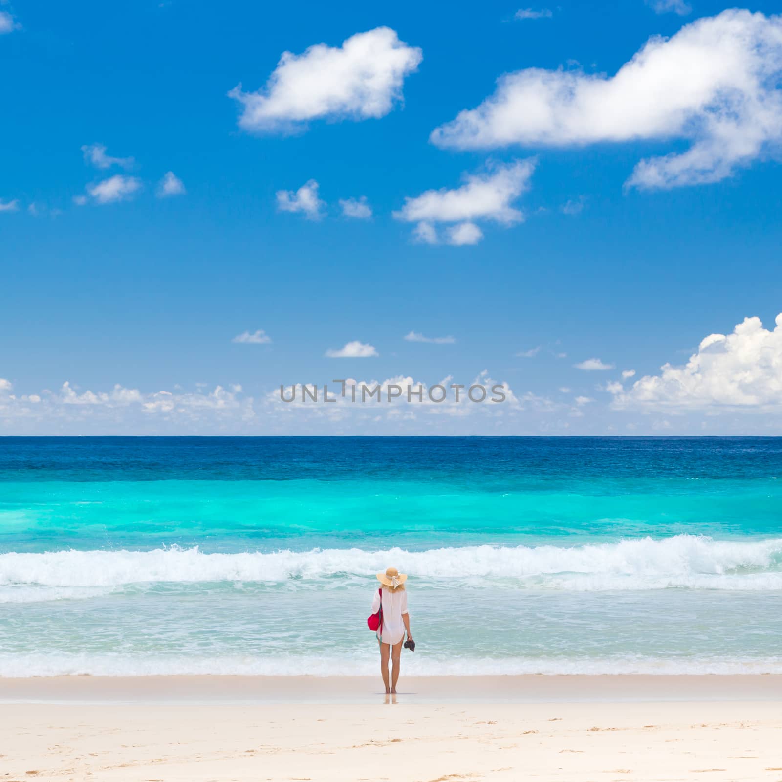 Woman wearing white tunic and beach hat, enjoying amazing view of Police Bay on Mahe Island, Seychelles. Summer vacations on picture perfect tropical beach concept.