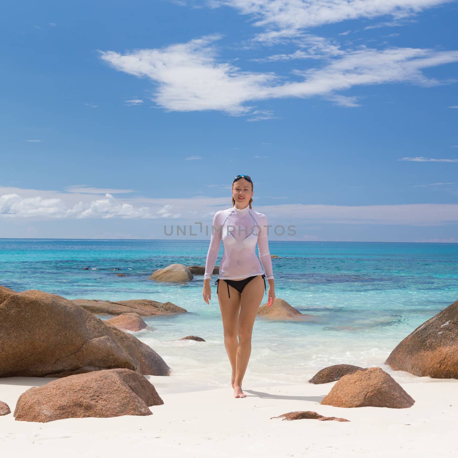 Woman wearing stylish bikini and lycra top enjoying swimming and snorkeling at amazing Anse Lazio beach on Praslin Island, Seychelles. Summer vacations on picture perfect tropical beach concept.