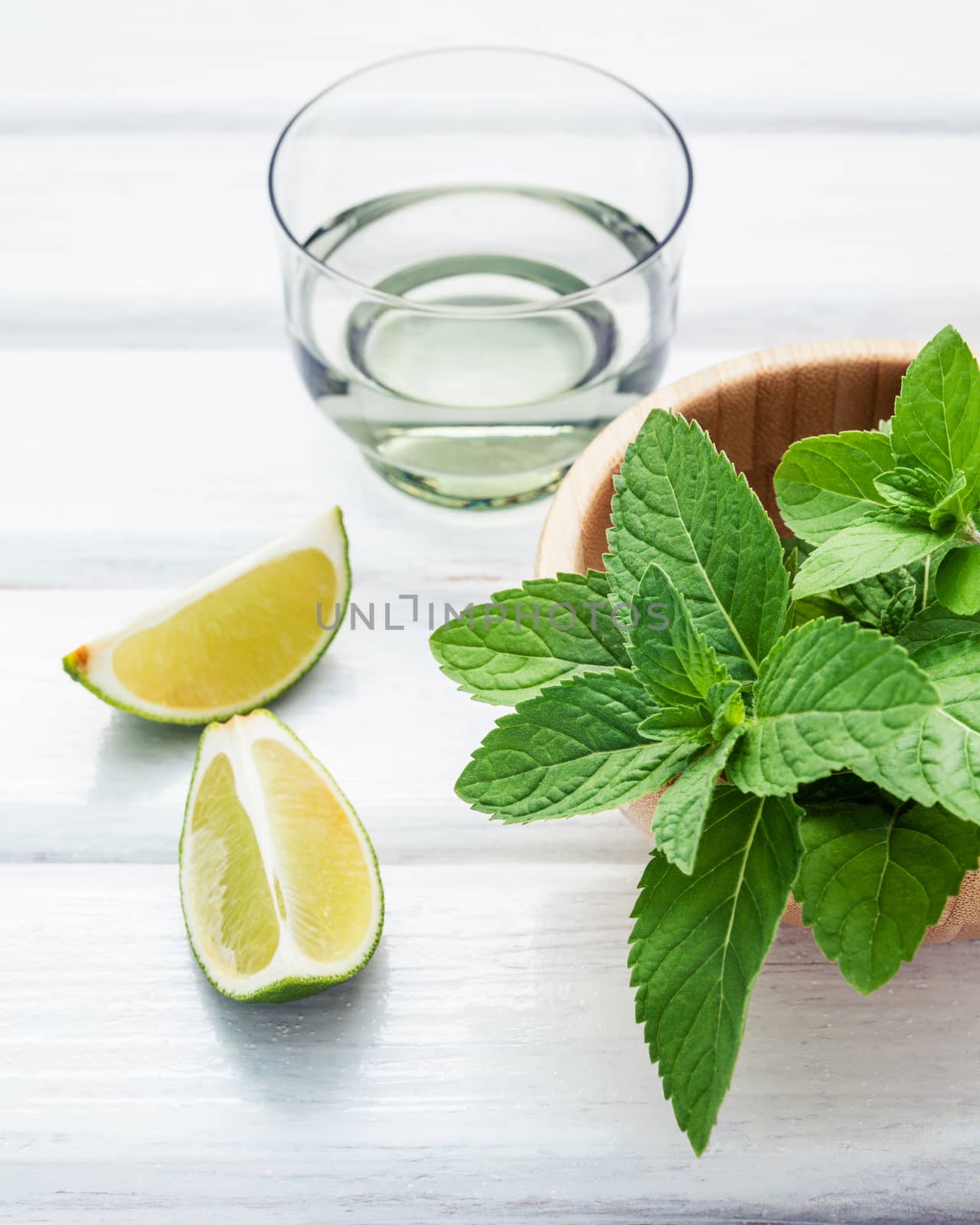 Ingredients for making mojito peppermint leaves, lime slices and vodka on white wooden table background. Selective focus shallow depth of field .