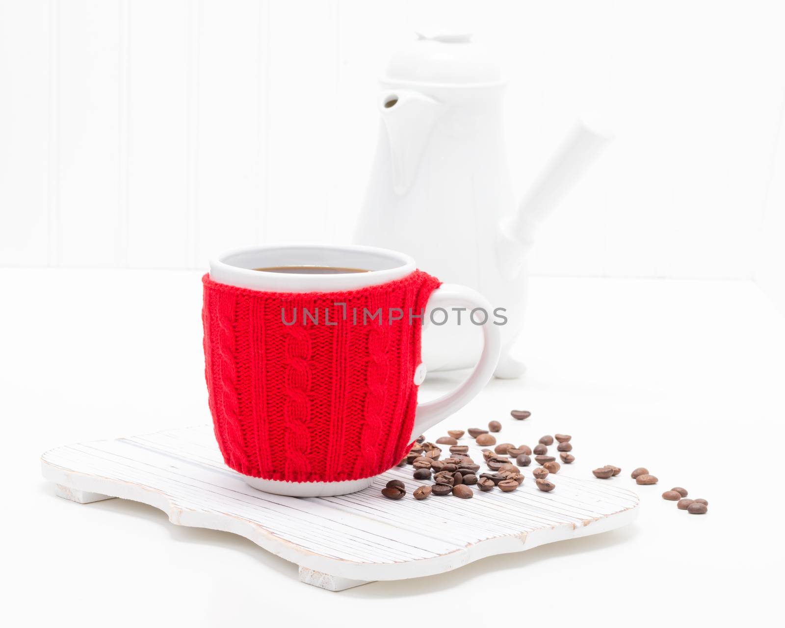 Cup of fresh brewed coffee in a cup with a bright red knitted cozy.