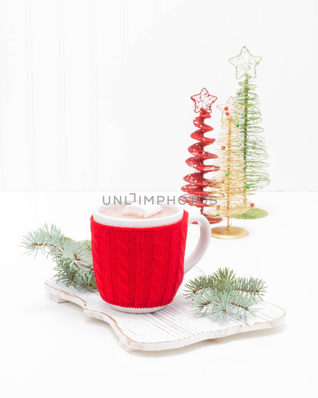 Hot chocolate in a white ceramic cup with a red cozy to keep it warm.