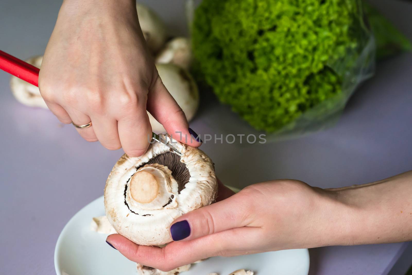hands clean mushrooms with a knife over a white plate