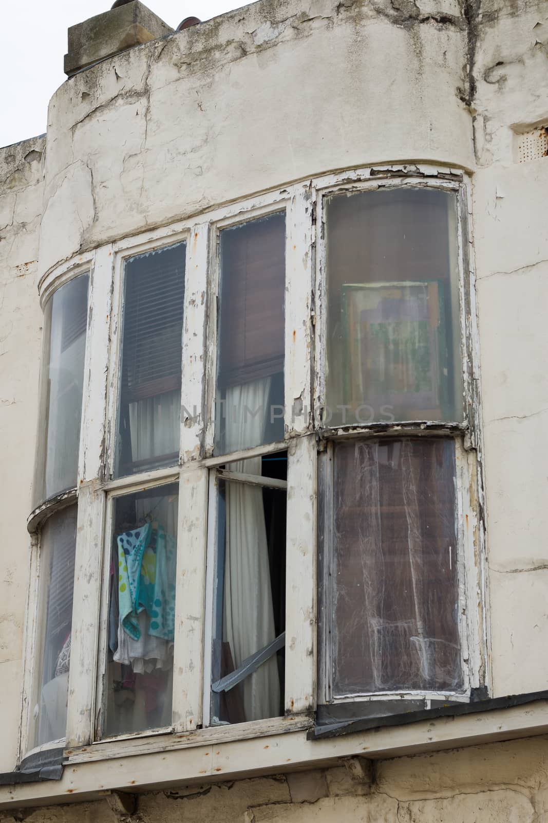 Neglected building with structural damage and broken window. View of squalid room.