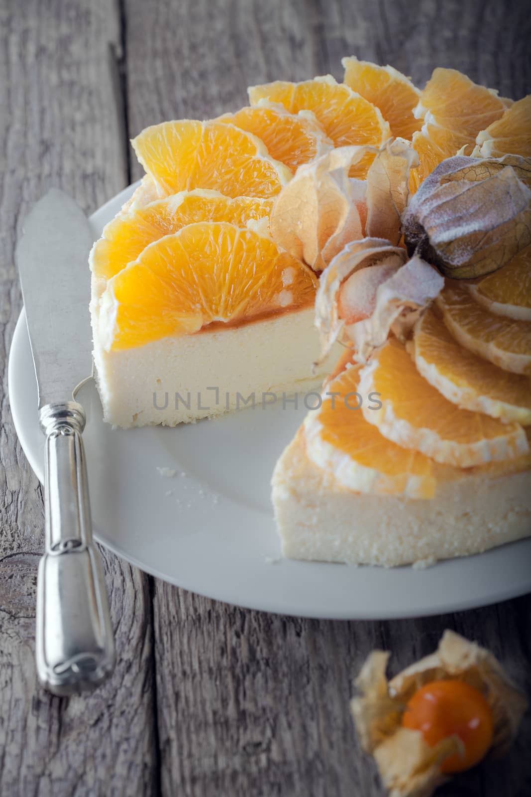 Cheesecake decorated with oranges and physalis on a plate.