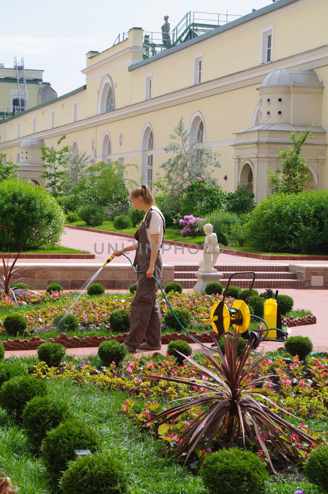 SAINT PETERSBURG, RUSSIA - JUNE 05, 205: woman gardener watering flowers in the garden of Hermitage major art museum. by evolutionnow