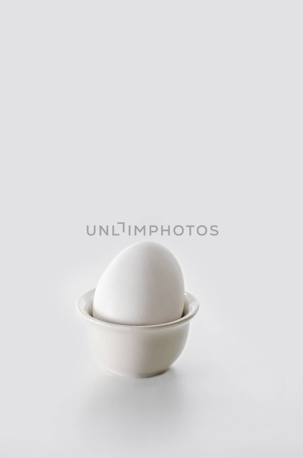 Egg in shell on stand, white background. High key, selective focus.