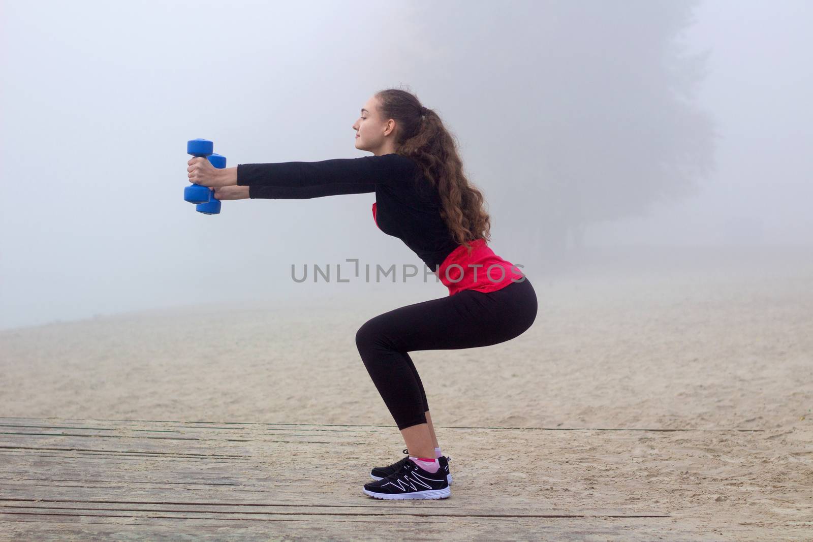 Young pretty slim fitness sporty woman exercises with weights dumbells during training workout outdoor