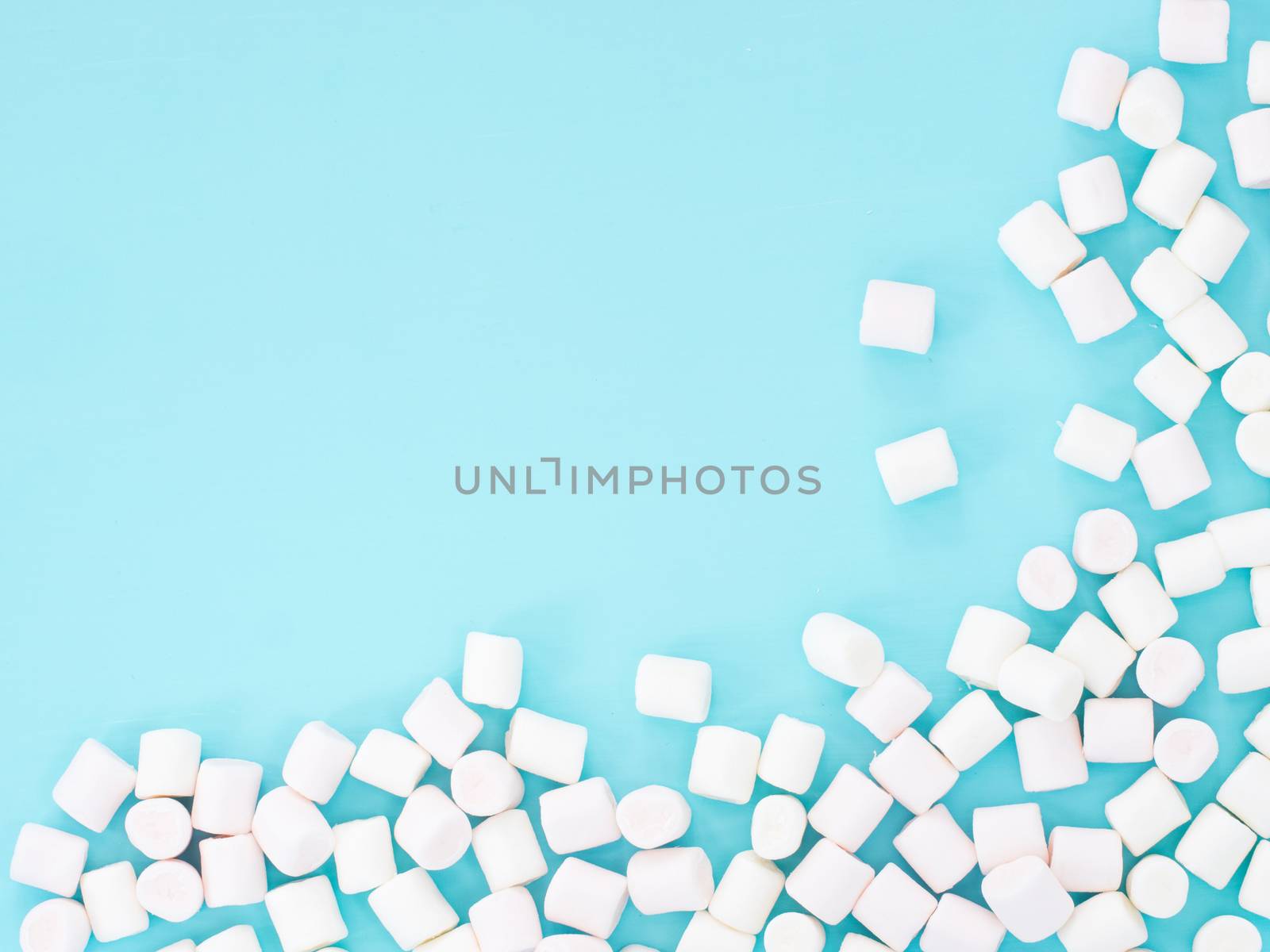 Marshmallows on blue background with copyspace. Flat lay or top view. Background or texture of colorful mini marshmallows.