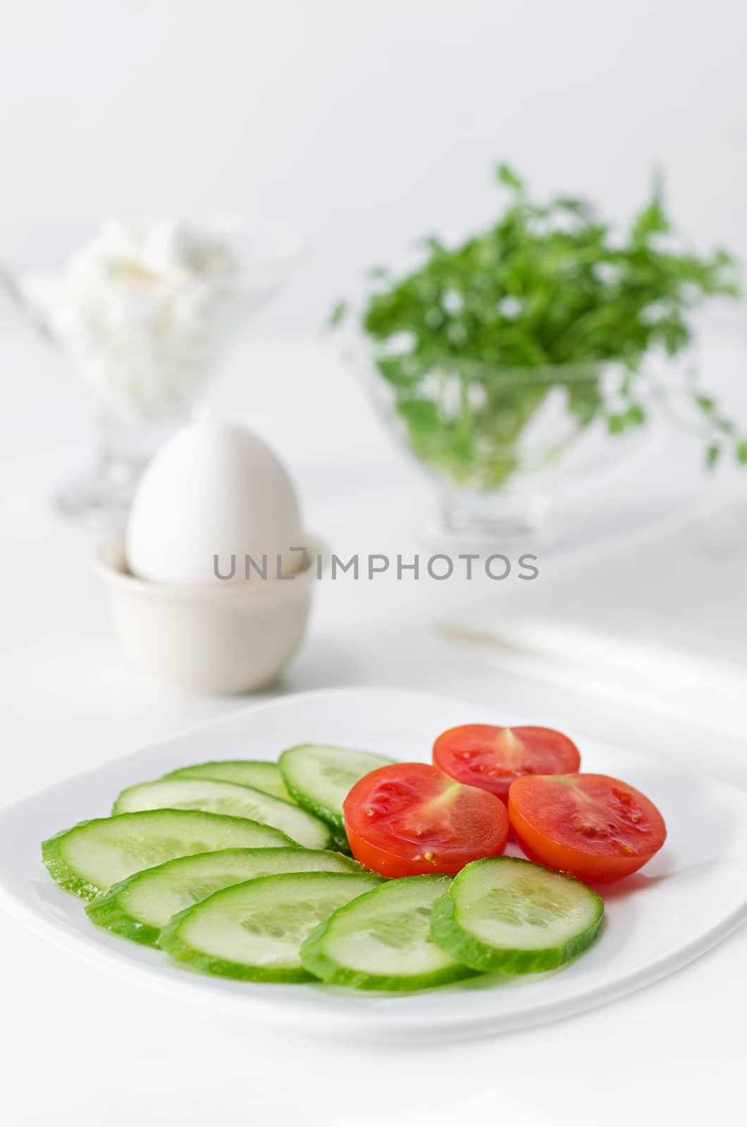 Sliced tomato and cucumber on a plate,  white background. High key, selective focus. by Gaina