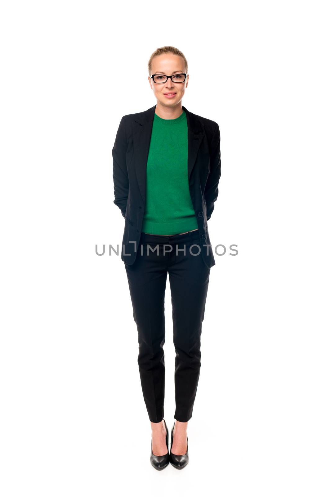 Full body portrait of beautiful smart young businesswoman in business attire wearin black eyeglasses, standing with arms behind her back against white background.