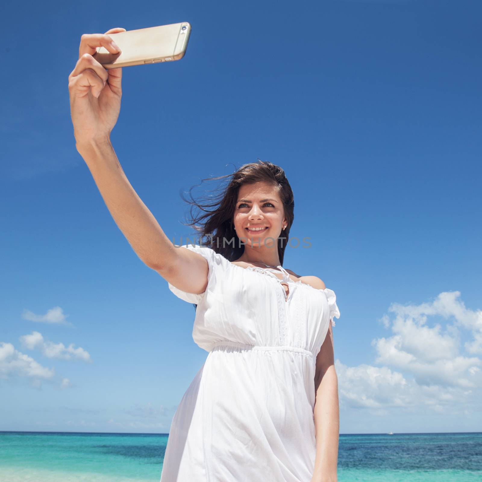 Smiling young woman taking selfie with smartphone on beach