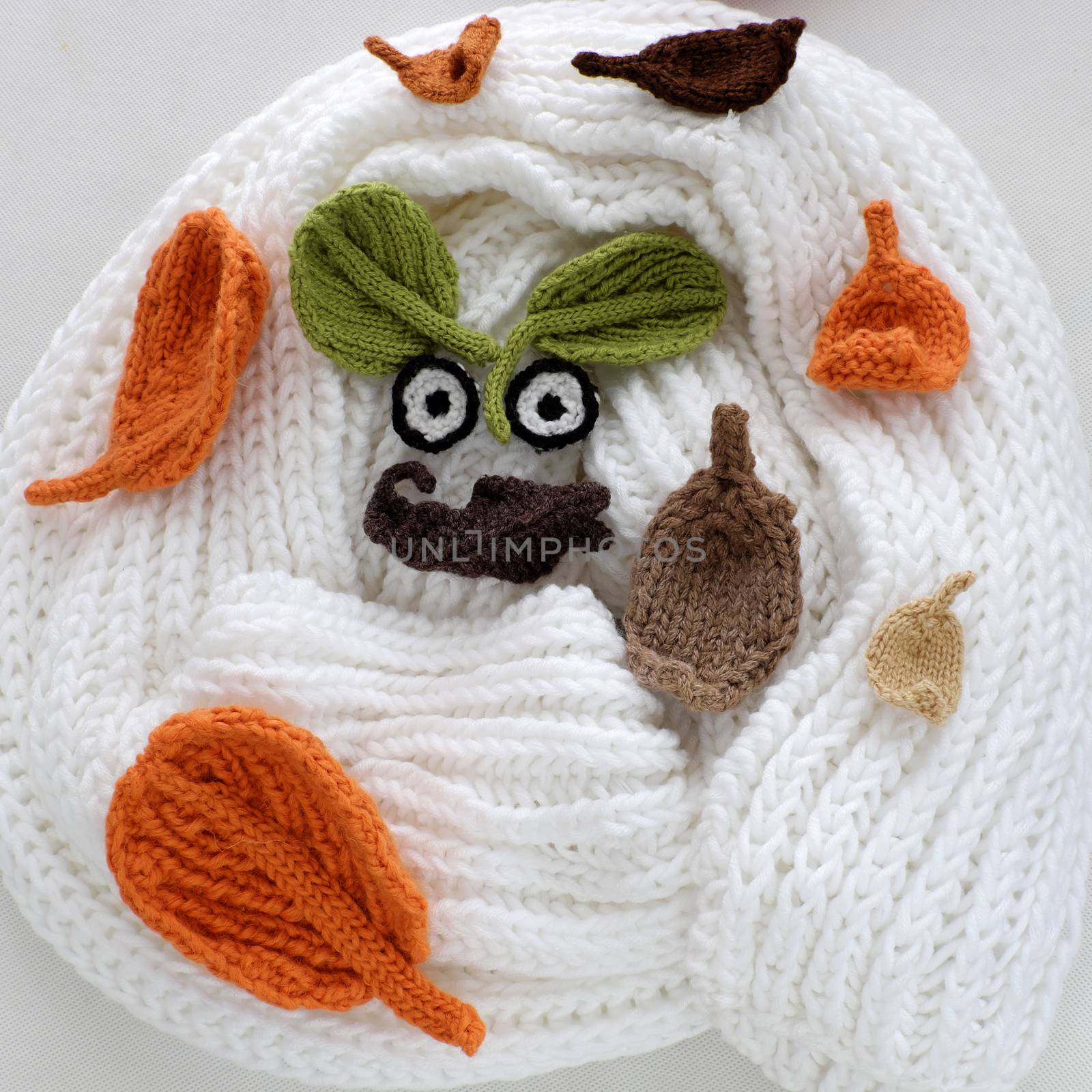 Humor eyes of winter make from yarn, diy simple background for Xmas holiday by knitted leaf for eyebrow, nose on white scarf background, joyful craft with funny face