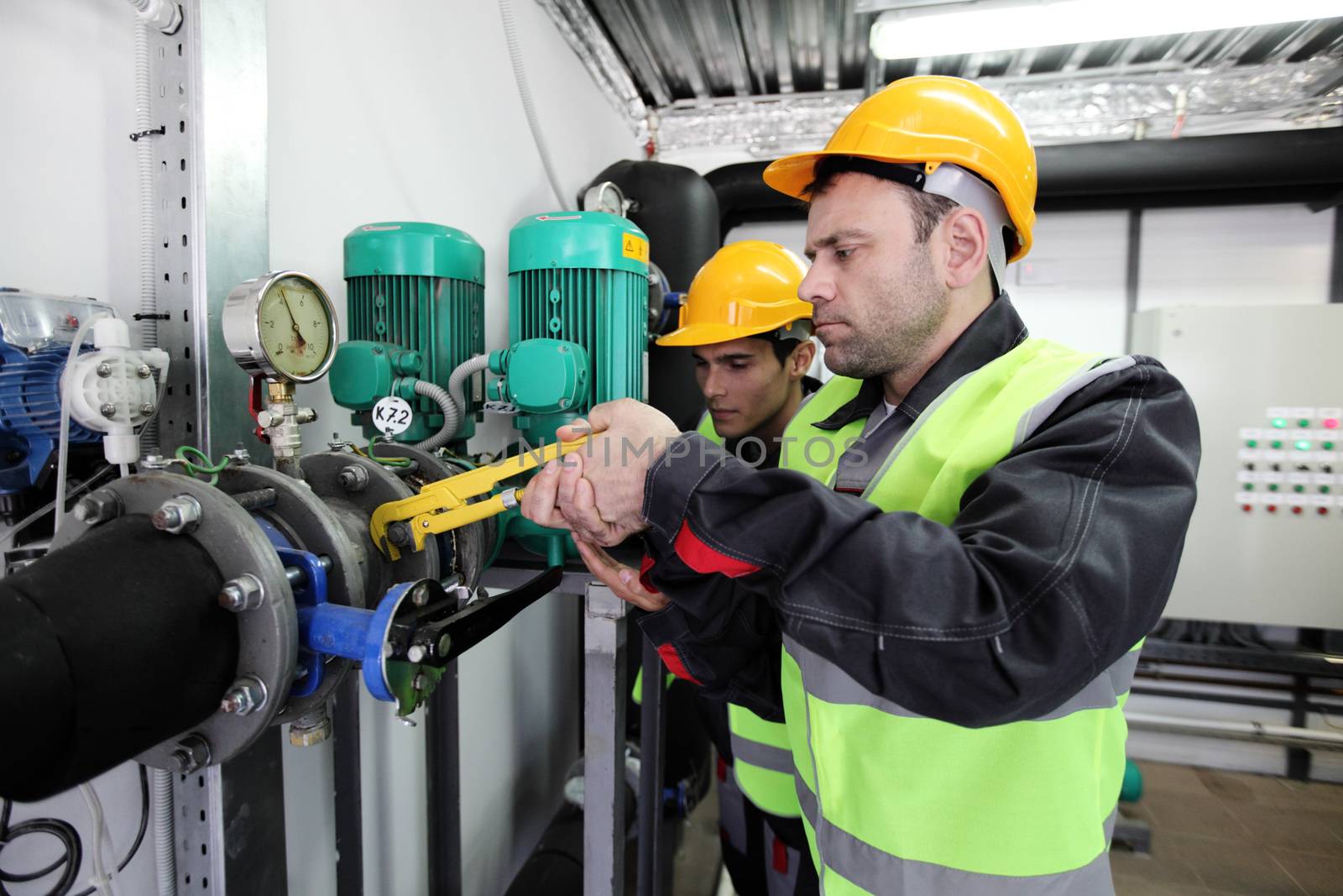 Two workers fixing pipes with manometer on high pressure system at factory