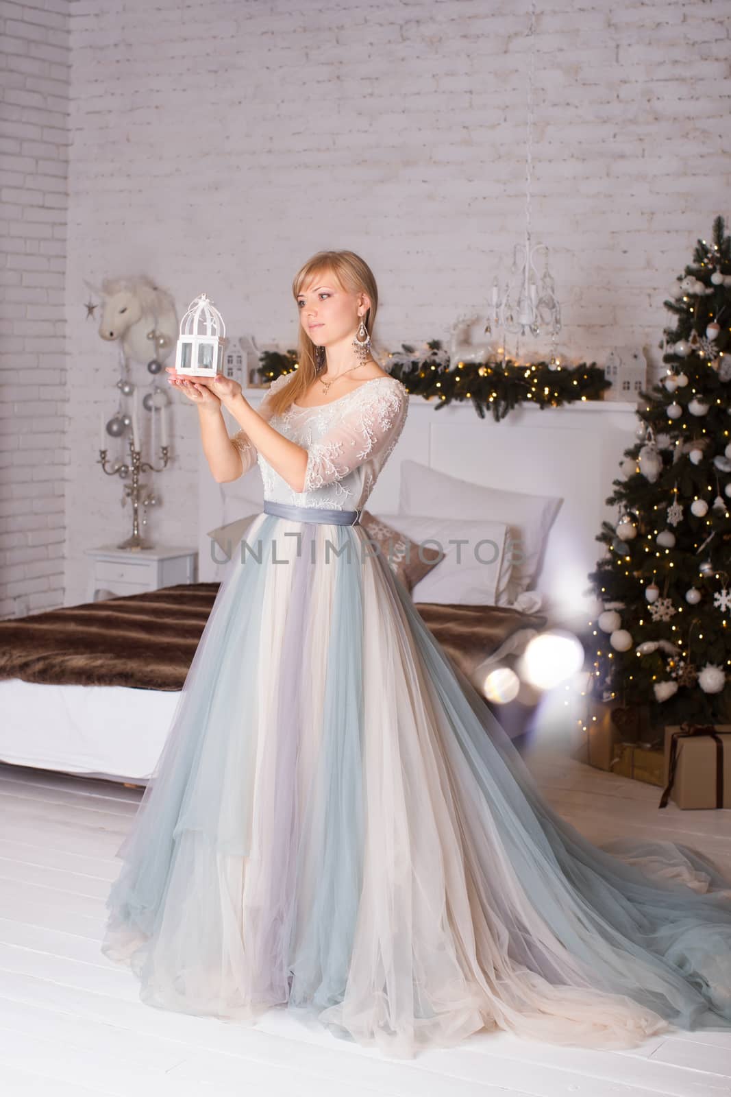 Girl in stylish dress holding a Christmas lantern in hand standing near trees