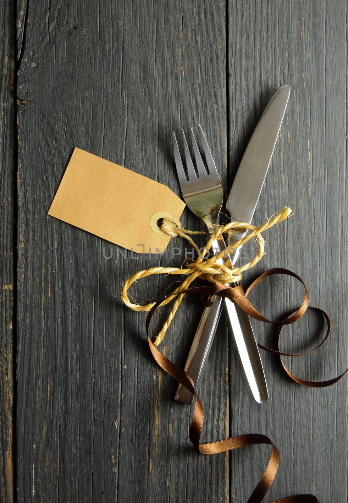 Fork and knife tied together on a wooden table background with tag