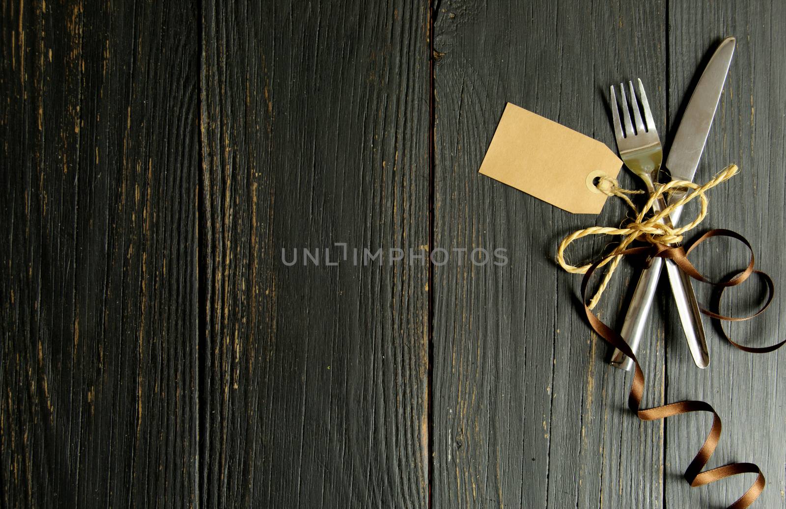 Fork and knife tied together on a wooden table background with tag