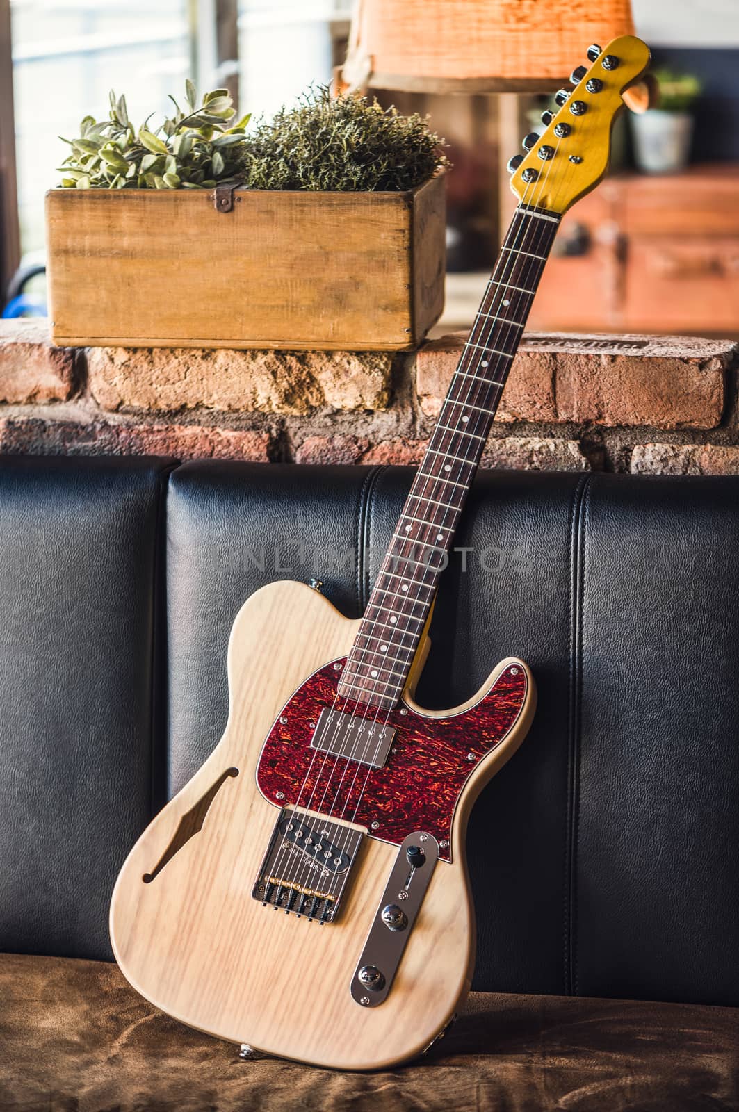 Electric Guitar Leaning Against a Couch. Electric Guitar with Natural Wood Finish Still Life.