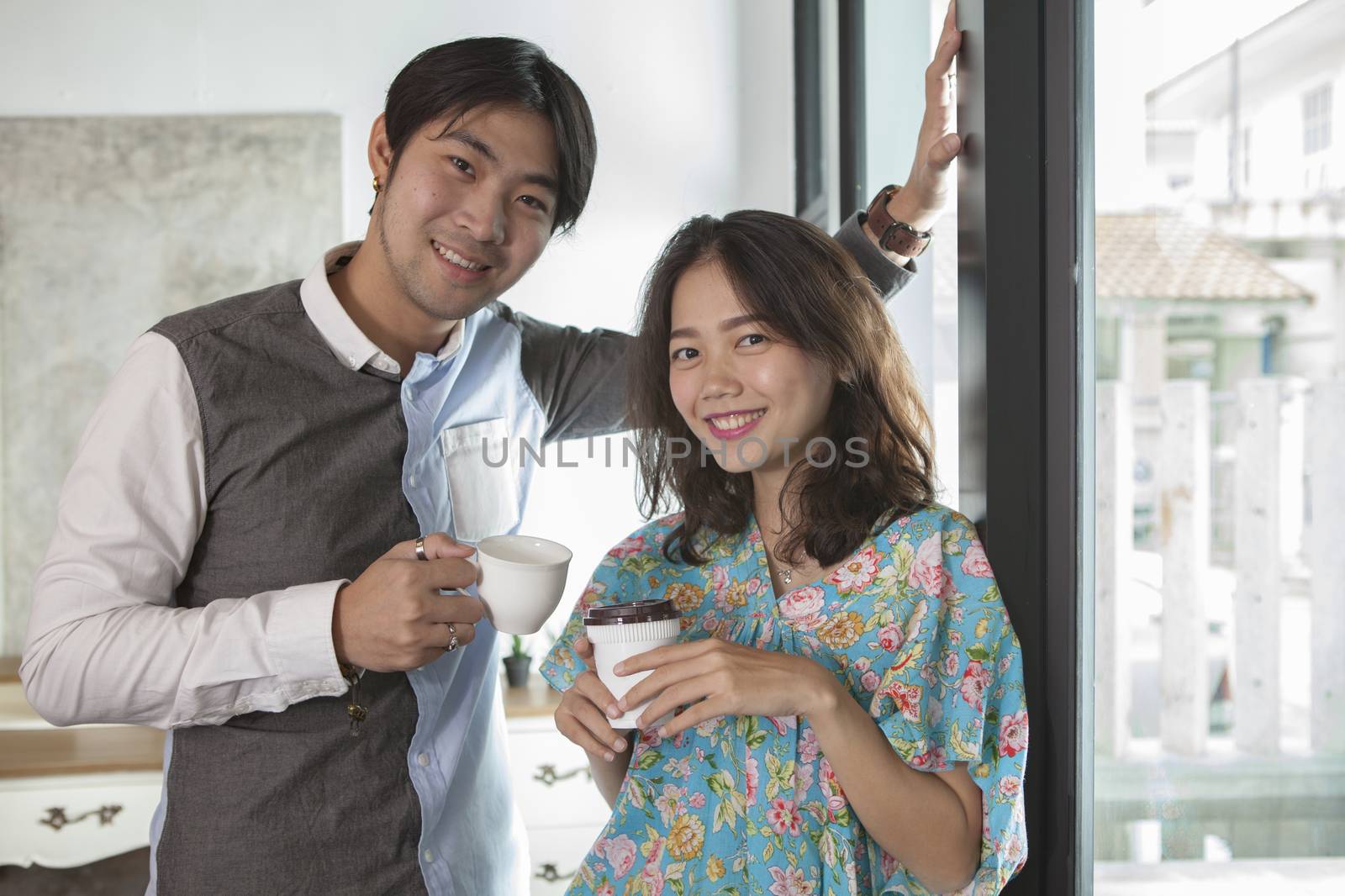 couples of asian young man and woman with coffee cup in hand standing relaxing in home living room