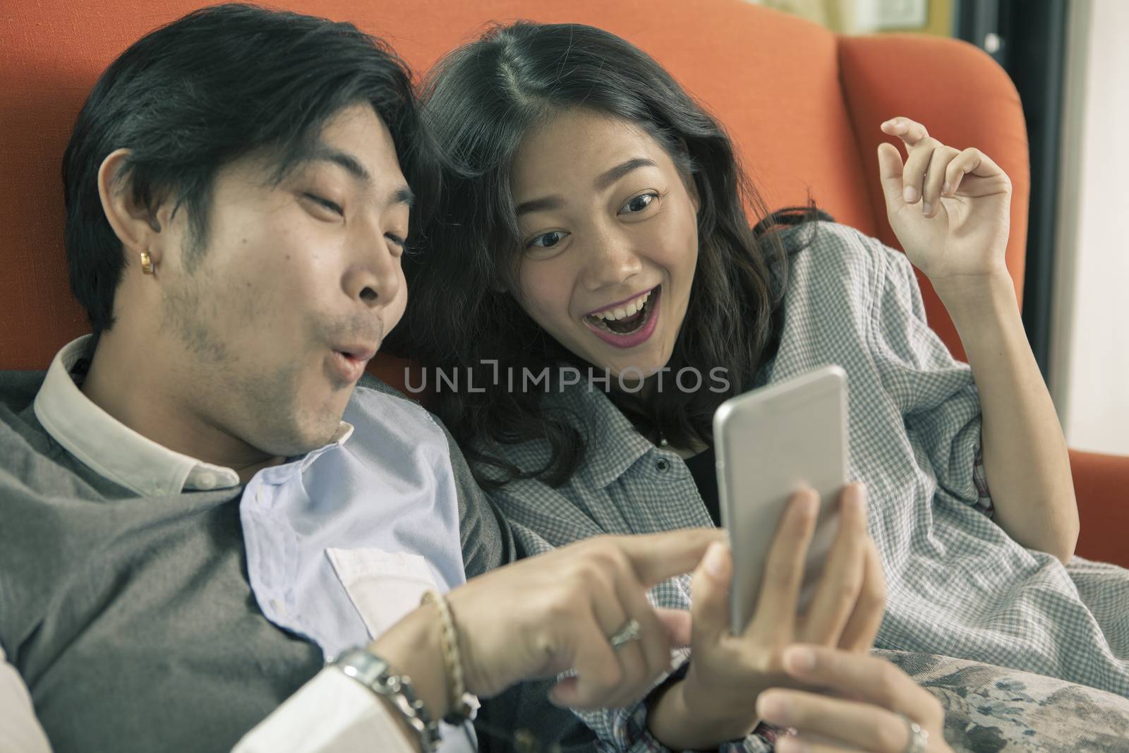 asian younger man and woman watching on smart phone with surpris by khunaspix