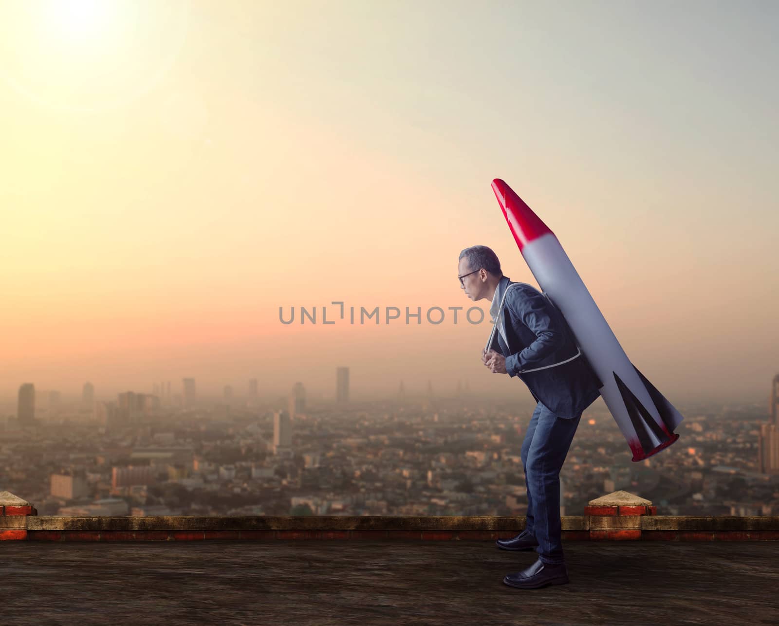 business man carries rocket missile on high building roof  against skyscraper scene for business conceptual