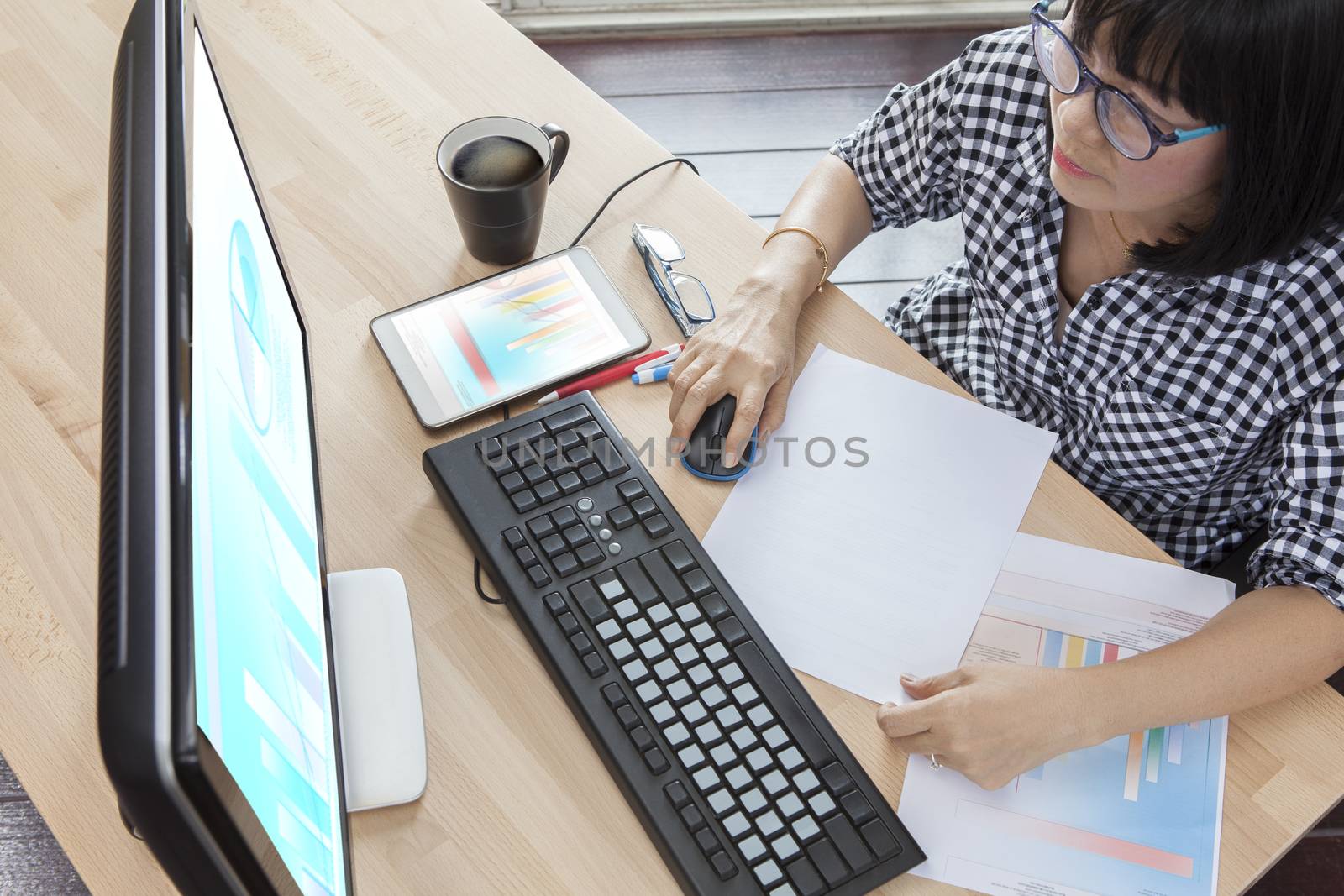 working woman with smart phone in hand looking to computer business report on table top