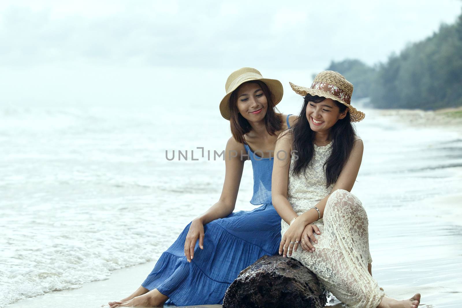 portrait of young beautiful asian tan skin woman wearing fashion straw hat sitting on wood lock at sea beach with relaxing emotion